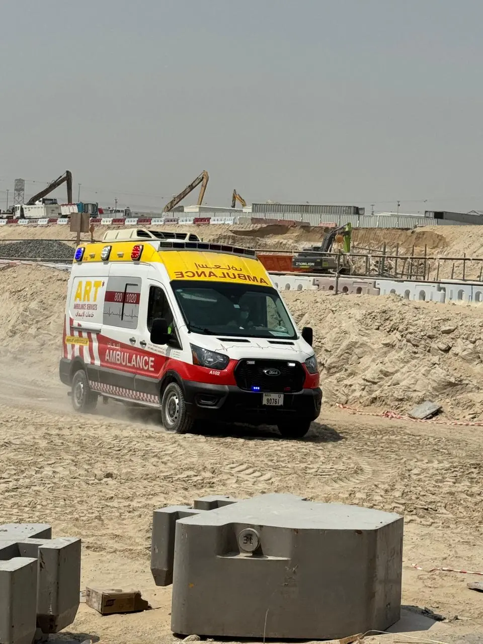 An ART ambulance driving across sand on a Dubai construction site, with excavators and site cabins behind