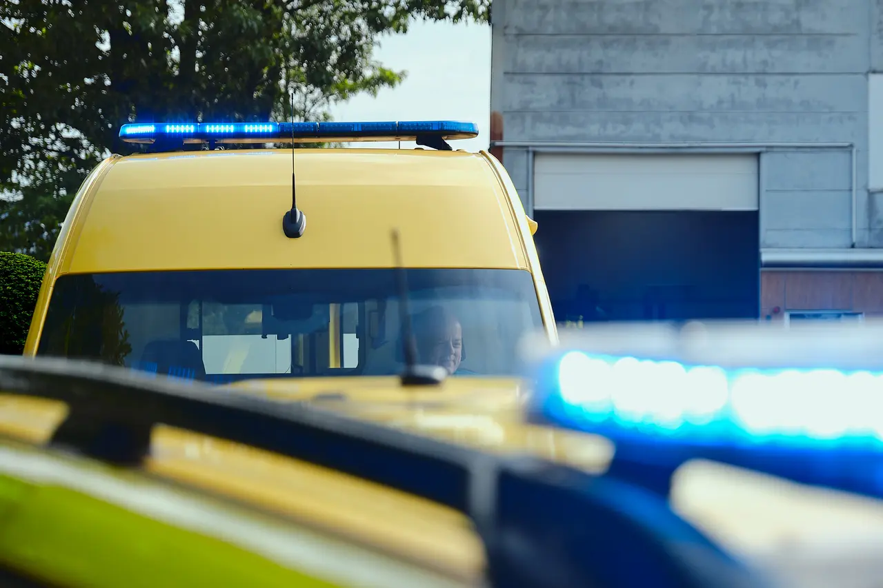 Two ambulances with blue emergency lights active, one facing the camera with the driver visible through the windscreen
