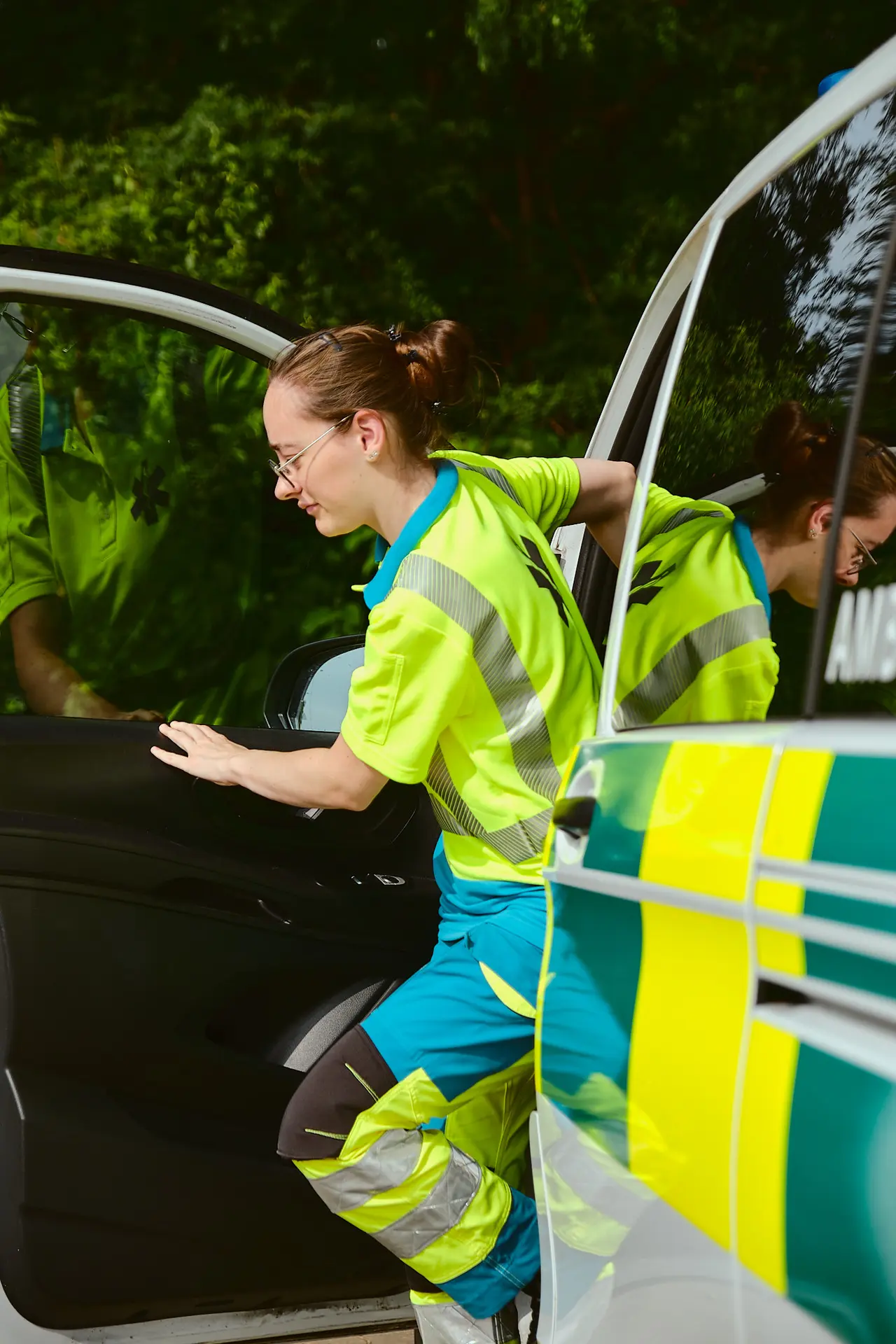 A paramedic in a high-visibility uniform stepping out of a rapid-response ambulance vehicle